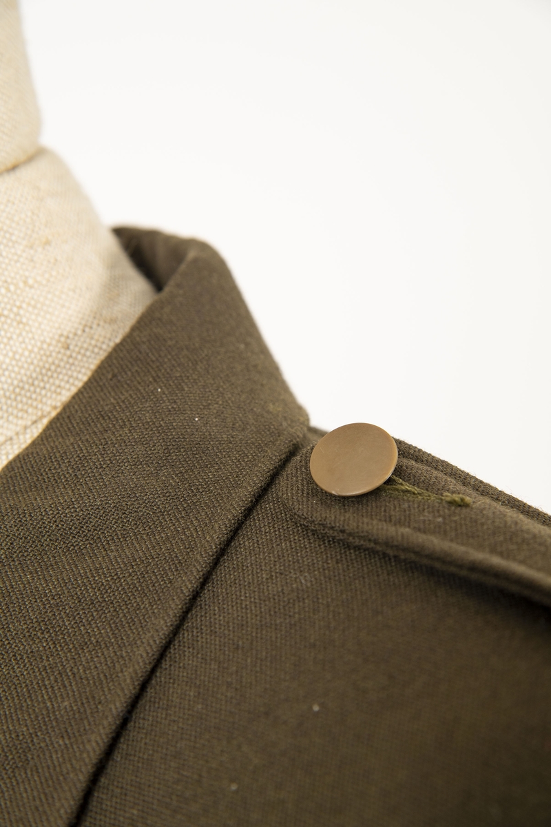 Uniform i flere deler:
a) Jakke. Påsydd rødt merke på ventre skulder:  UNRRA. Etikett i nakken: Size 18 R. En stripe rundt ermene, enkeltspent, brystlommer og to innstikklommer. Krage og slag. Skulderklaffer. Plastknapper.
b) Skjørt. Rett skjørt, midtsøm foran og bak. smal linning, glidelås i siden. Tilstand: falden tatt opp, brunt bendelbånd nederst. 
c) Båtlue. Brunt polyesterfor. Etikett: 23. Utvisket stempel i sølv. 
d) Et par sokker. Ull, militær brungrønn.Ribbestrikket, glatt hel og såle.
e-g) Tre lommetørklær. Bomull, militær brune.