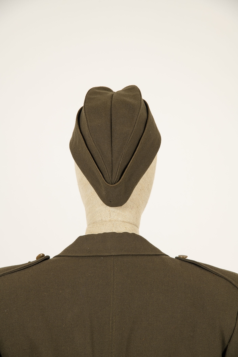 Uniform i flere deler:
a) Jakke. Påsydd rødt merke på ventre skulder:  UNRRA. Etikett i nakken: Size 18 R. En stripe rundt ermene, enkeltspent, brystlommer og to innstikklommer. Krage og slag. Skulderklaffer. Plastknapper.
b) Skjørt. Rett skjørt, midtsøm foran og bak. smal linning, glidelås i siden. Tilstand: falden tatt opp, brunt bendelbånd nederst. 
c) Båtlue. Brunt polyesterfor. Etikett: 23. Utvisket stempel i sølv. 
d) Et par sokker. Ull, militær brungrønn.Ribbestrikket, glatt hel og såle.
e-g) Tre lommetørklær. Bomull, militær brune.