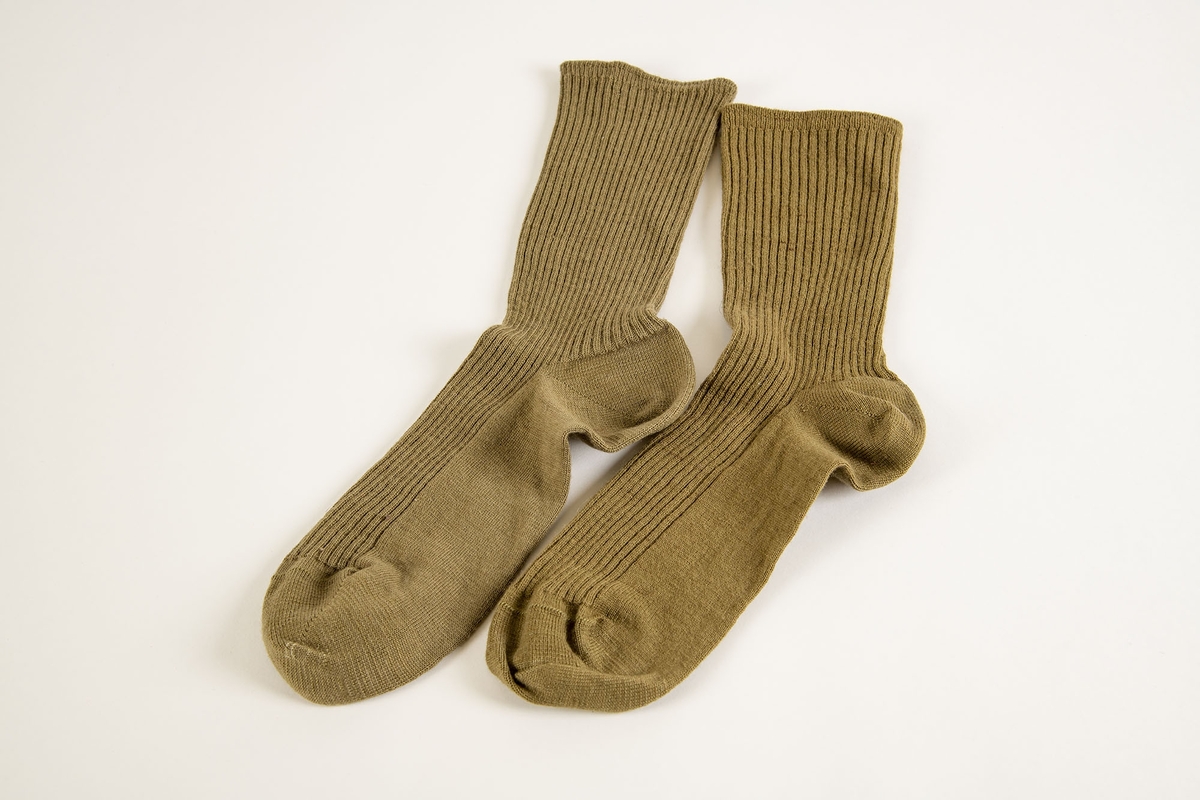Uniform i flere deler:
a) Jakke. Påsydd rødt merke på ventre skulder:  UNRRA. Etikett i nakken: Size 18 R. En stripe rundt ermene, enkeltspent, brystlommer og to innstikklommer. Krage og slag. Skulderklaffer. Plastknapper.
b) Skjørt. Rett skjørt, midtsøm foran og bak. smal linning, glidelås i siden. Tilstand: falden tatt opp, brunt bendelbånd nederst. 
c) Båtlue. Brunt polyesterfor. Etikett: 23. Utvisket stempel i sølv. 
d) Et par sokker. Ull, militær brungrønn.Ribbestrikket, glatt hel og såle.
e-g) Tre lommetørklær. Bomull, militær brune.