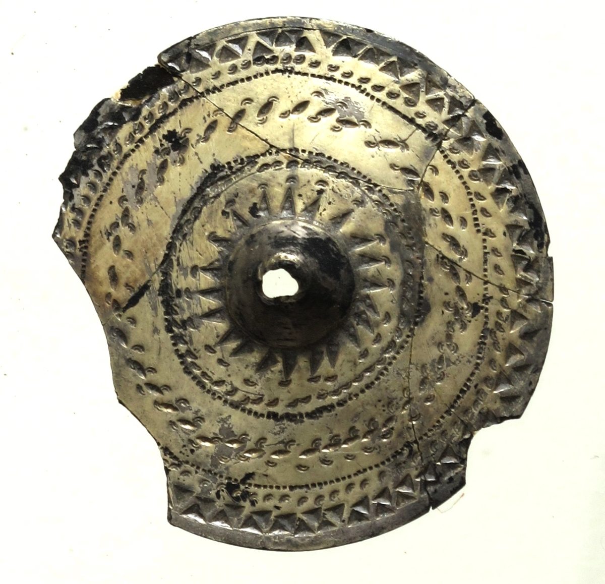 Sirkelrund plate med konisk midtknopp av forgylt sølv av typen [Rygh fig.310]R. 310. Stykket er ornert med konsentriske felter med punsel- og stempelornering, nemlig en dobbelt rad trekanter, så en rekke med små punkter, en tredobbelt rad med noe større punkter og halvmåner på hver side begrenset av en småstiplet linje. Midtstykket er omgitt av en rad sterkt tilspissete trekanter ved hvis toppunkter det finnes små halvmåner. Den ytre begrensning er her en rad små punkter. Stykkets kant er glatt. Foreligger i 5 sammenhørende deler. Noe av kanten mangler. 
