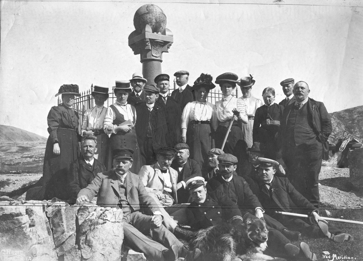 Passasjerene fra DS Andenæs (1903) poserer foran Meridianstøtten på Fuglenes i Hammerfest