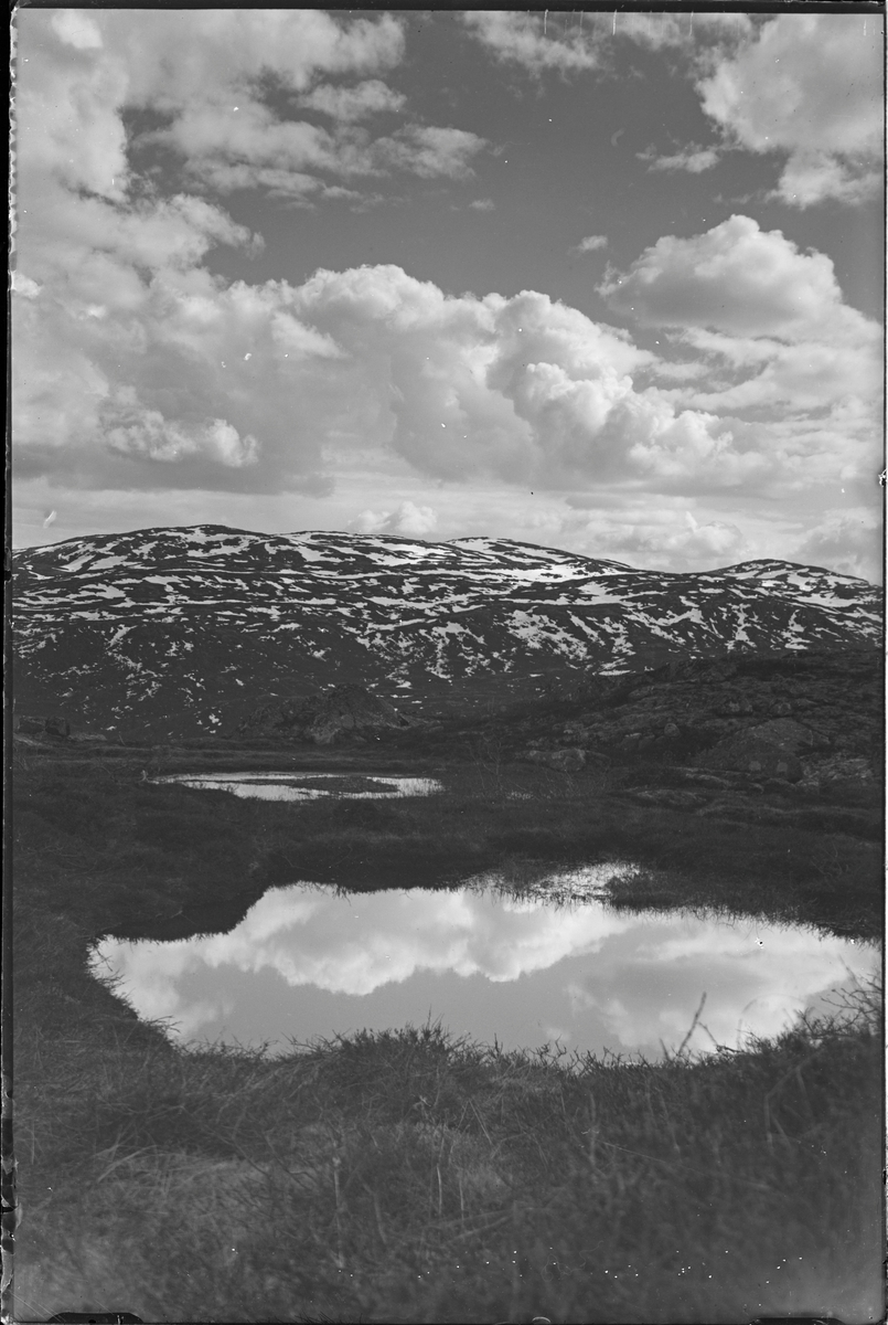 Vann i fjellandskap. Fjelltopper rundt med snøflekker på.