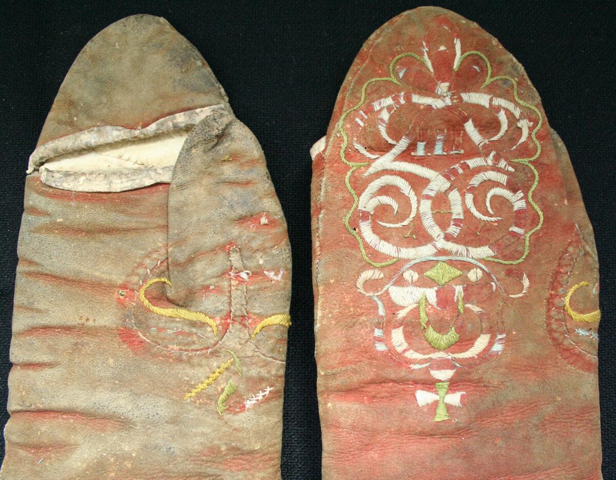 Kvinnohandskar. Rödfärgade skinnhandskar med vit ullsida inåt. Öppning i handens och i tummens insida som kantats med vitt skinn. Broderi av silke på handrygg och tumme. Motiv Gustaf III spegelmonogram och slingor. 

/Elisabet Johansson 2019.