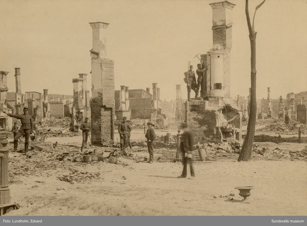 Sundsvalls stadsbrand 1888. Militären hjälper till i arbetet att röja i brandresterna och endast kakelugnarna finns kvar av husen som tidigare stått på platsen.