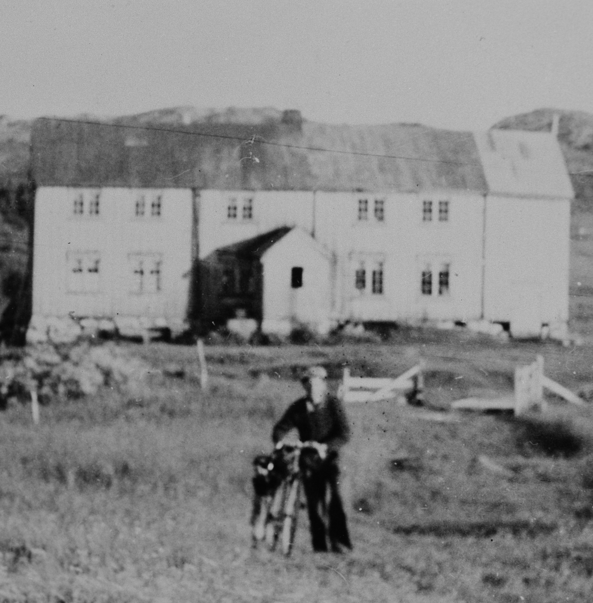 Mann står ved siden av en sykkel, bygning i bakgrunnen.