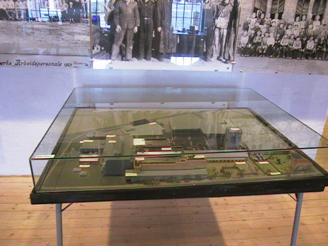 Rektangulær modell på 4 bein med glassmonter over. Modellen gir en oversikt over fabrikkområdet på Glassverkstomta i Moss.