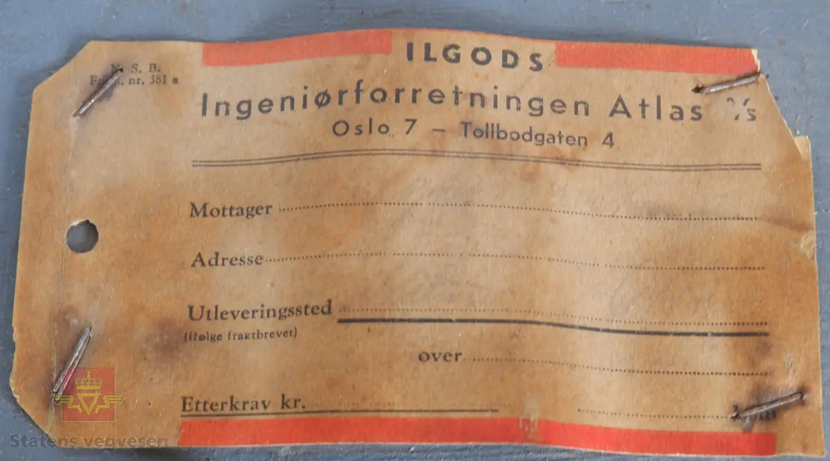 Ei trakt og et 10 liters målekar i aluminium. Ei glassplate samt bruksanvisninger i ei malt trekasse. Delene er kontrollmåler, trakt og 10 liters målekar. I lokket er det et rom for medfølgende glassplate.