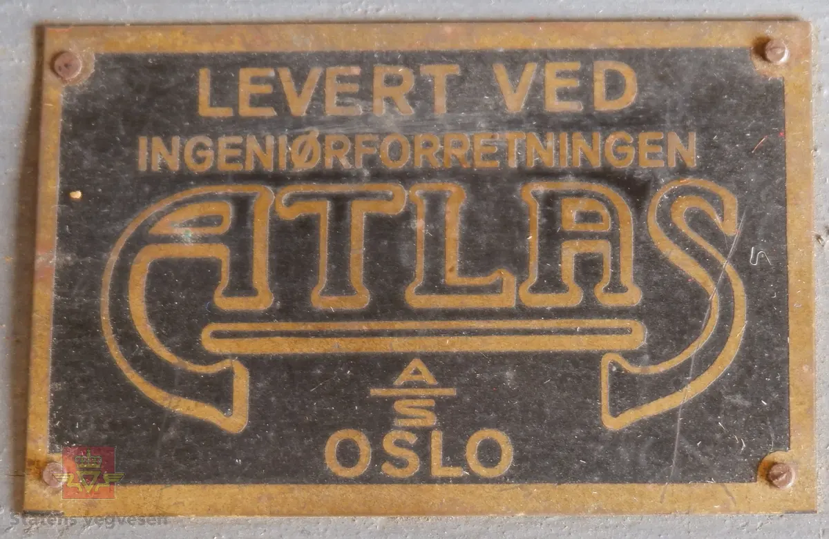 Ei trakt og et 10 liters målekar i aluminium. Ei glassplate samt bruksanvisninger i ei malt trekasse. Delene er kontrollmåler, trakt og 10 liters målekar. I lokket er det et rom for medfølgende glassplate.