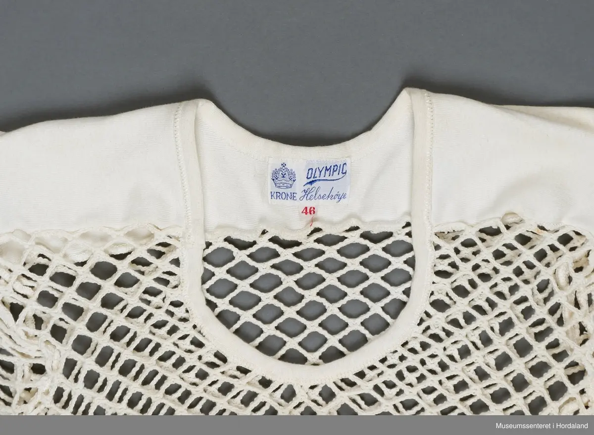 Krone Olympic helseundertrøye med korte erme i str. 46. Trøya har rund hals og skulderstykke i tettvevd bomullsstoff, elles helsetrøyestoff med svært store hol.