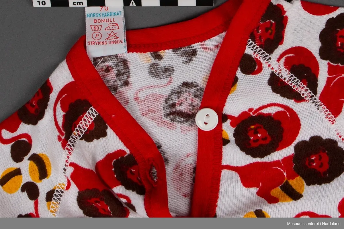 Plagget: Løver med ball i brunt, rødt og gult.
Emballasjen: Fargefoto av baby.