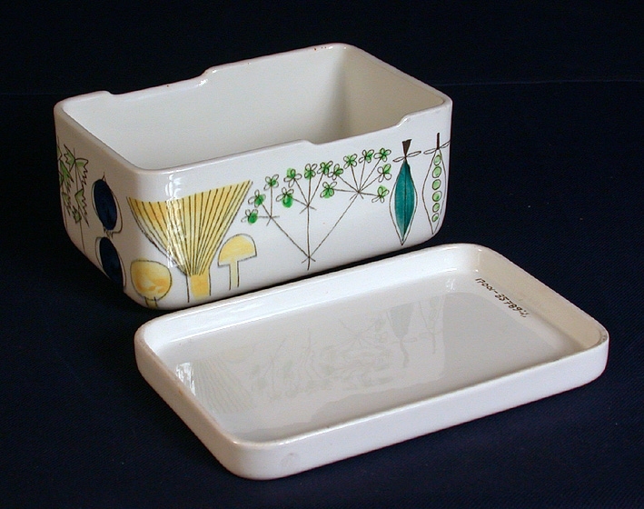 Rektangulär porslinsask med polykrom dekor med vitt, slätt lock. Asken har 2 st nedsänkningar snett mittemot varandra på askens långsidor.