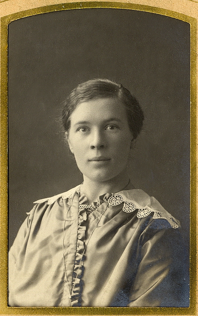 En kvinna i blus med spetskantad vit krage.
Under fotot text med blyerts: "Helga Jarl".
Bröstbild, halvprofil. Ateljéfoto.