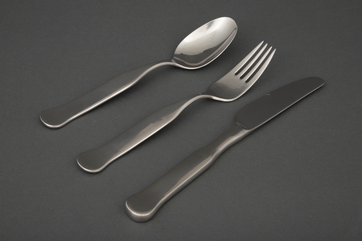 Middagsbestikksett i presset rustfritt stål, bestående av tre deler.

1) Bordkniv med smalt knivblad med små tagger. Skaftet tiltar i bredde og er rett frem til skaftenden som er bredere og avrundet. 
2) Spisegaffel med smalt, ovalt gaffelblad med fire tinner. Skaftet er smalt ved roten og tiltar i bredde og er rett frem til skaftenden som er bredere og avrundet. 
3) Spiseskje med ovalt skjeblad. Skaftet er smalt ved roten, tiltar i bredde og er rett frem til skaftenden som er bredere og avrundet.