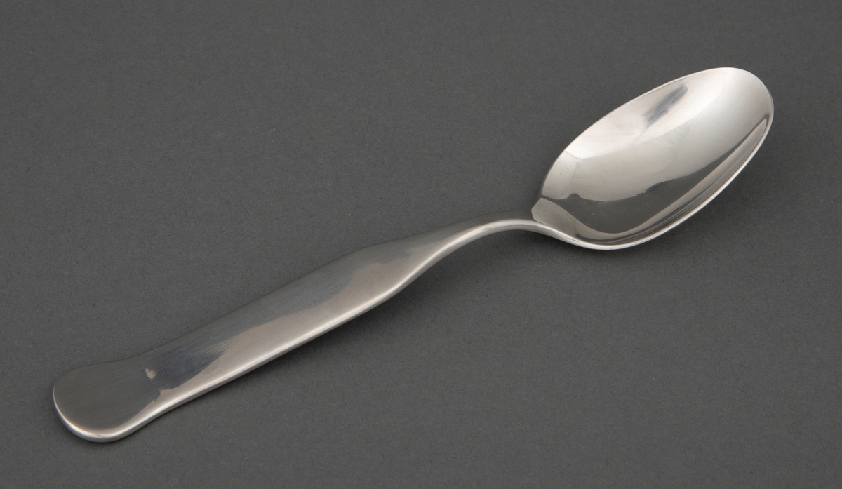 Spiseskje i presset, rustfritt stål med ovalt skjeblad. Skaftet er smalt ved roten og tiltar i bredde og er rett