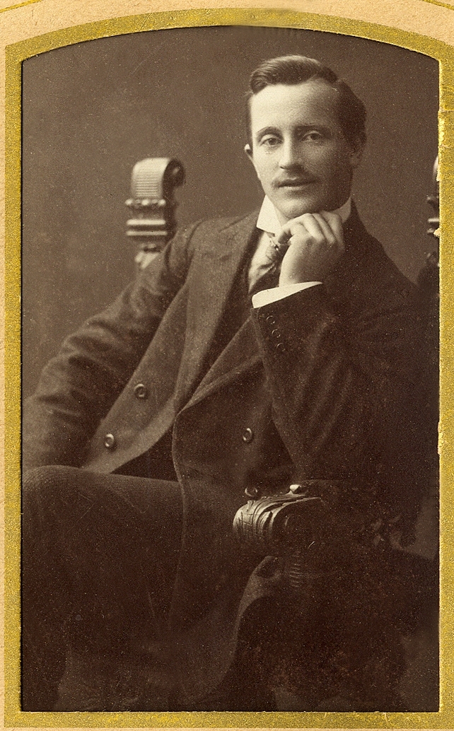 En man i kostym med väst, stärkkrage och slips, har intagit en tänkarpose i en karmstol hos fotografen.
Under fotot text med blyerts: "Gunnar Elg".
Knäbild, halvprofil. Ateljéfoto.