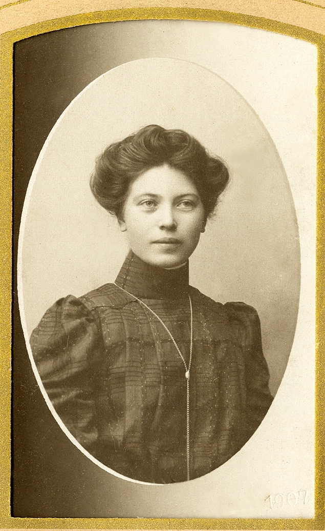 En ung okänd kvinna i mörk, höghalsad klänning med klockkedja och brosch vid halsen.
I nedre högra hörnet inpräglat årtal: "1907".
Bröstbild, halvprofil. Ateljéfoto.
