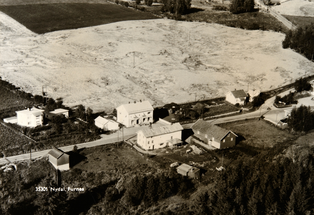 Postkort, Ringsaker, Furnes, flyfoto Nydal landhandleri og bakeri, Nydal Meieri rett over vegen, til høyre eindommen Onset og helt til høyre Furnes Bilcentral og bensinstasjon hvor drosjesjåførene Olaf Mæland, Teodor Engli og Kristian Kvarstad hadde holdeplass, 
(Nydal II, gnr/bnr 766/49)