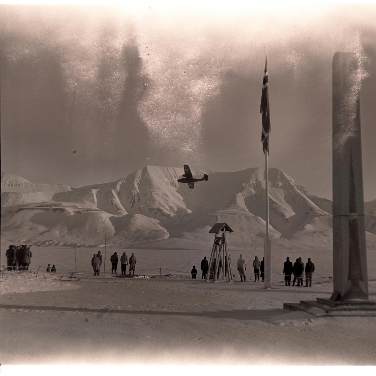 Postflyet dropper postsekker over myra i Longyearbyen 18.mars 1956. Folk som følger med fra bautaen på Skjæringa.