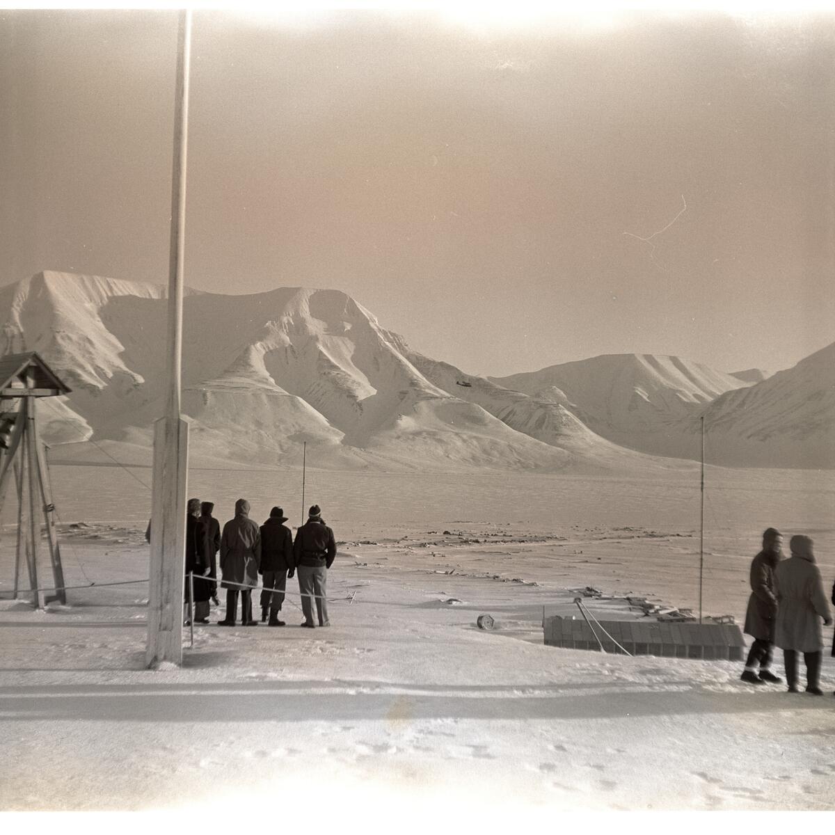 Postflyet dropper postsekker over myra i Longyearbyen 18.mars 1956. Folk som følger med fra bautaen på Skjæringa.