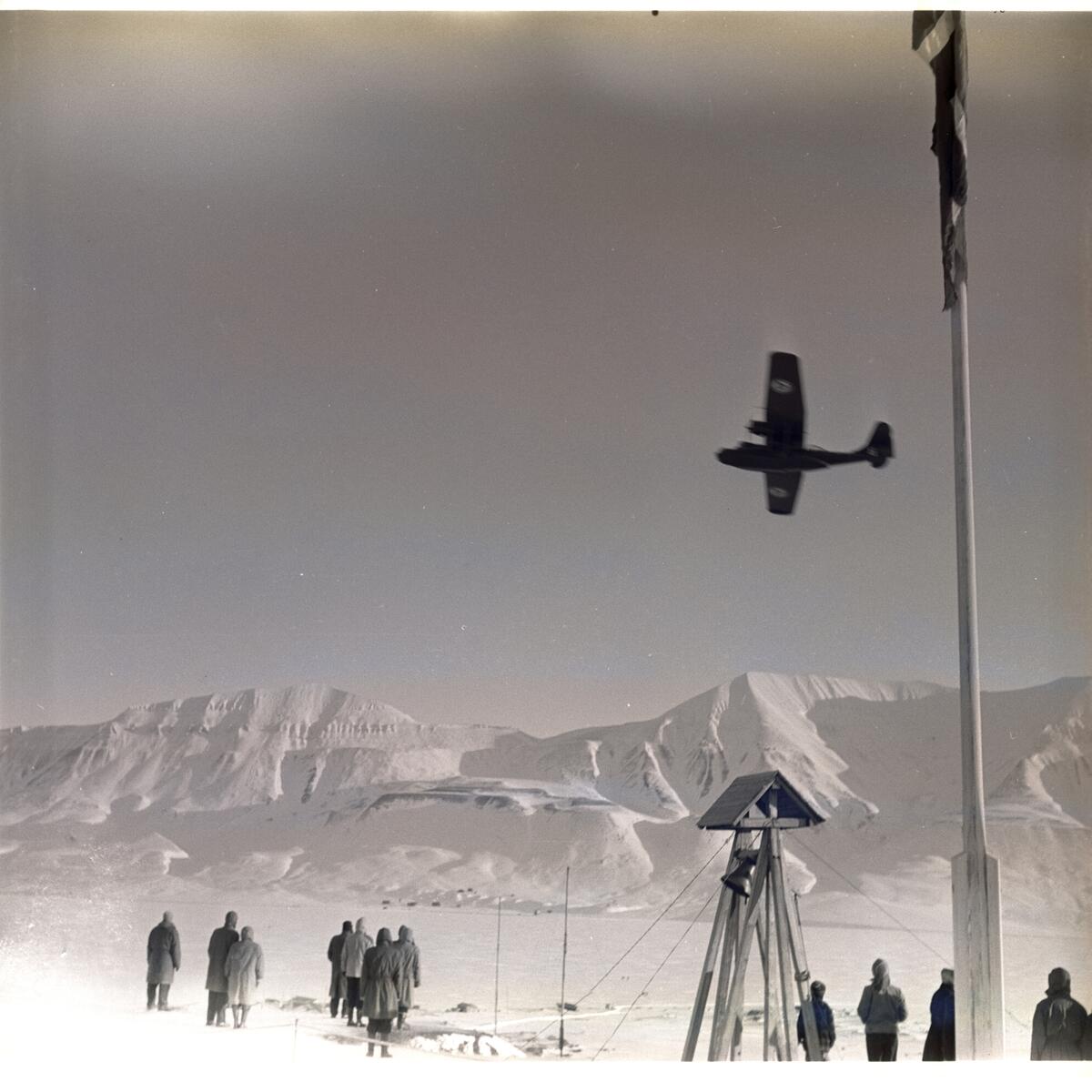 Postflyet dropper postsekker over myra i Longyearbyen 18.mars 1956. Folk som følger med fra bautaen på Skjæringa.