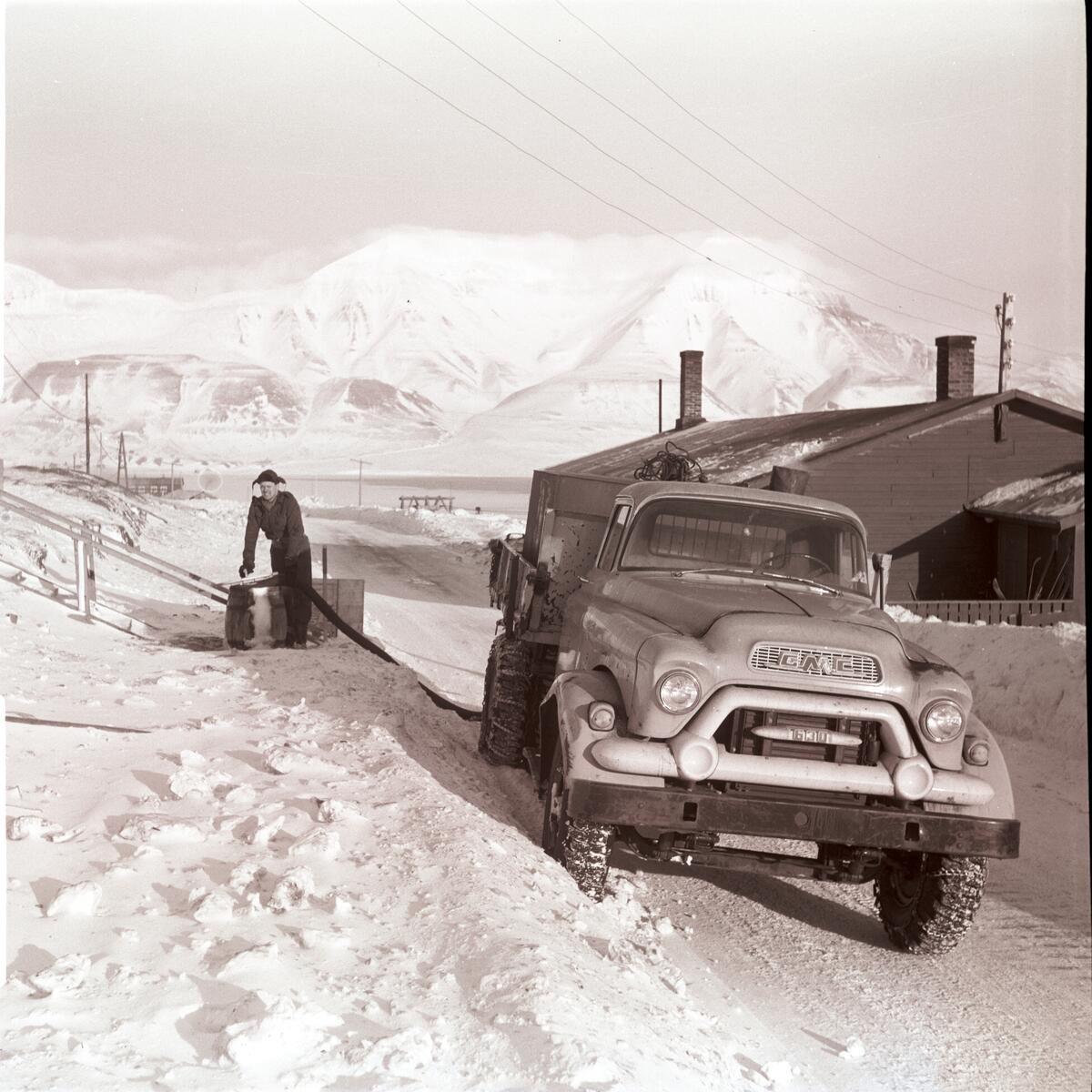 Isaksen på vannbilen/tankbilen kommer med vann til fjøsmesterboligen/gamlekontoret vinteren 1958. Fjørmesteren/røkteren bodde i det gamle kontoret like ovenfor bakeriet i Gamle Longyearbyen/Skjæringa.