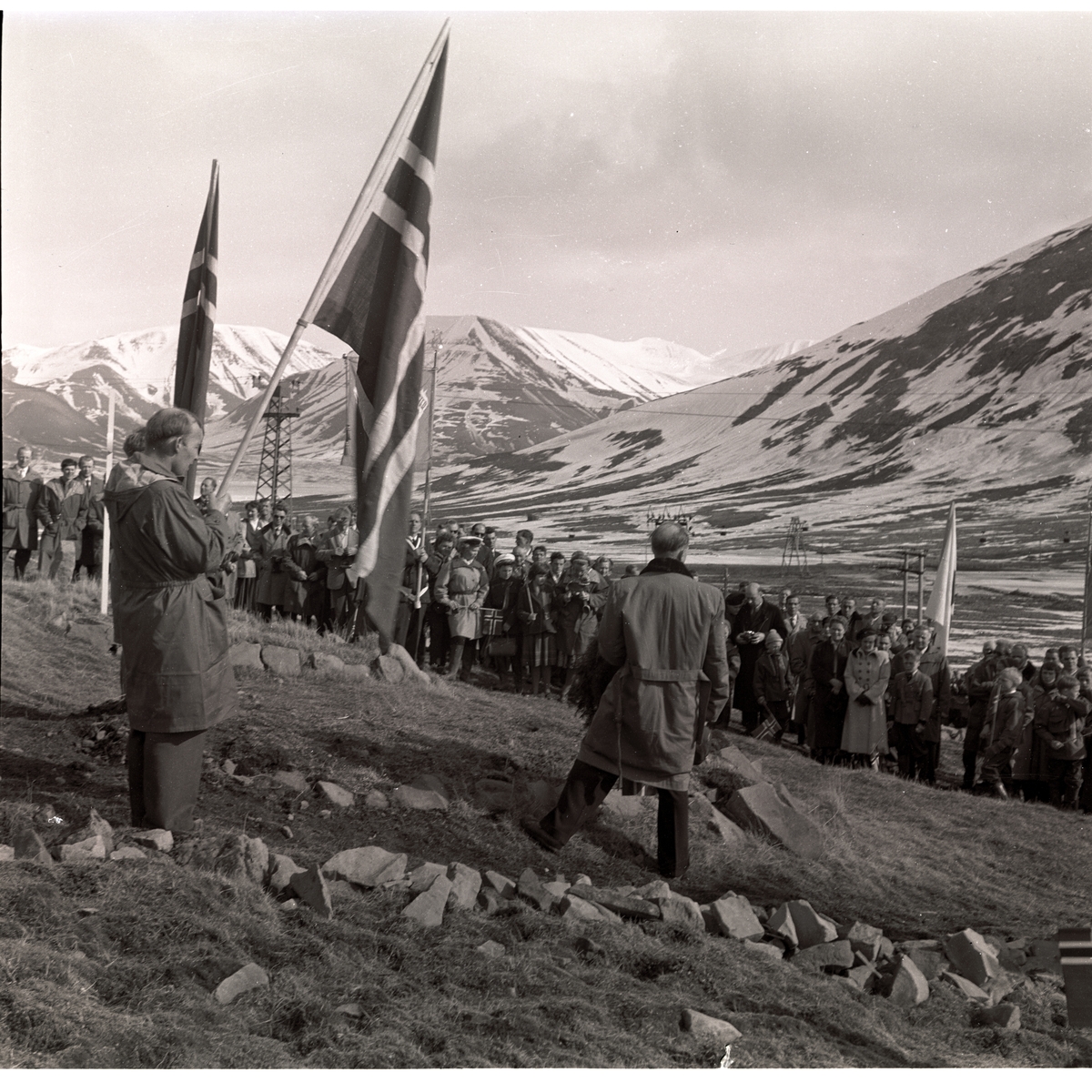 Kransenedlegging ved Richard Knutsen på Trond Astrup Vigtels  grav på kirkegården 17.mai 1957. Det sto tidligere et hvitt trekors på graven til Vigtel, men våren 1957 ble det byttet ut med en gravstein. Kaptein Vigtel var født i 1930, og falt på post under forsvaret av Longyearbyen under tyskernes angrep i september 1943. Forsvarsdepartementet sørget for at alle norske krigsgraver skulle ha gravstøtter av likt utseende, og presten Nødtvedt ble bedt om å besørge dette. Dette ble så markert 17.mai 1957. Richard Knutsen med ryggen til kamera, Tore Fure med flagg.  Ellers kan man se Bodil Langbakk, Nils Langbakk, Bergljot Langbakk, Bernt Tollefsen, Inger Anne Lund, Aud Strande, Solveig Nødtvedt, Trygve Hansen, Helene Hansen, Harald Grøndal (med kamera)