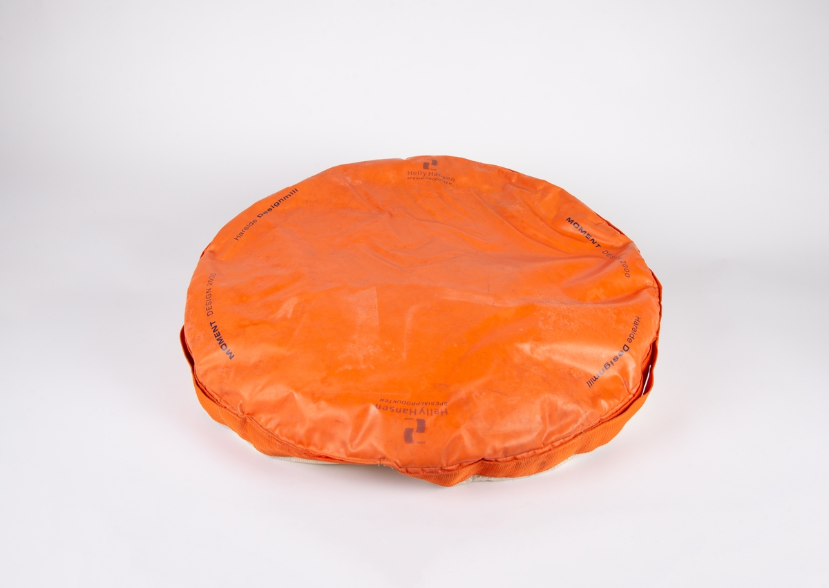 Sirkulær pute fylt med isoporkuler. Oransje underside og hvit overside.  Sort logo for Momentum Design på overside.