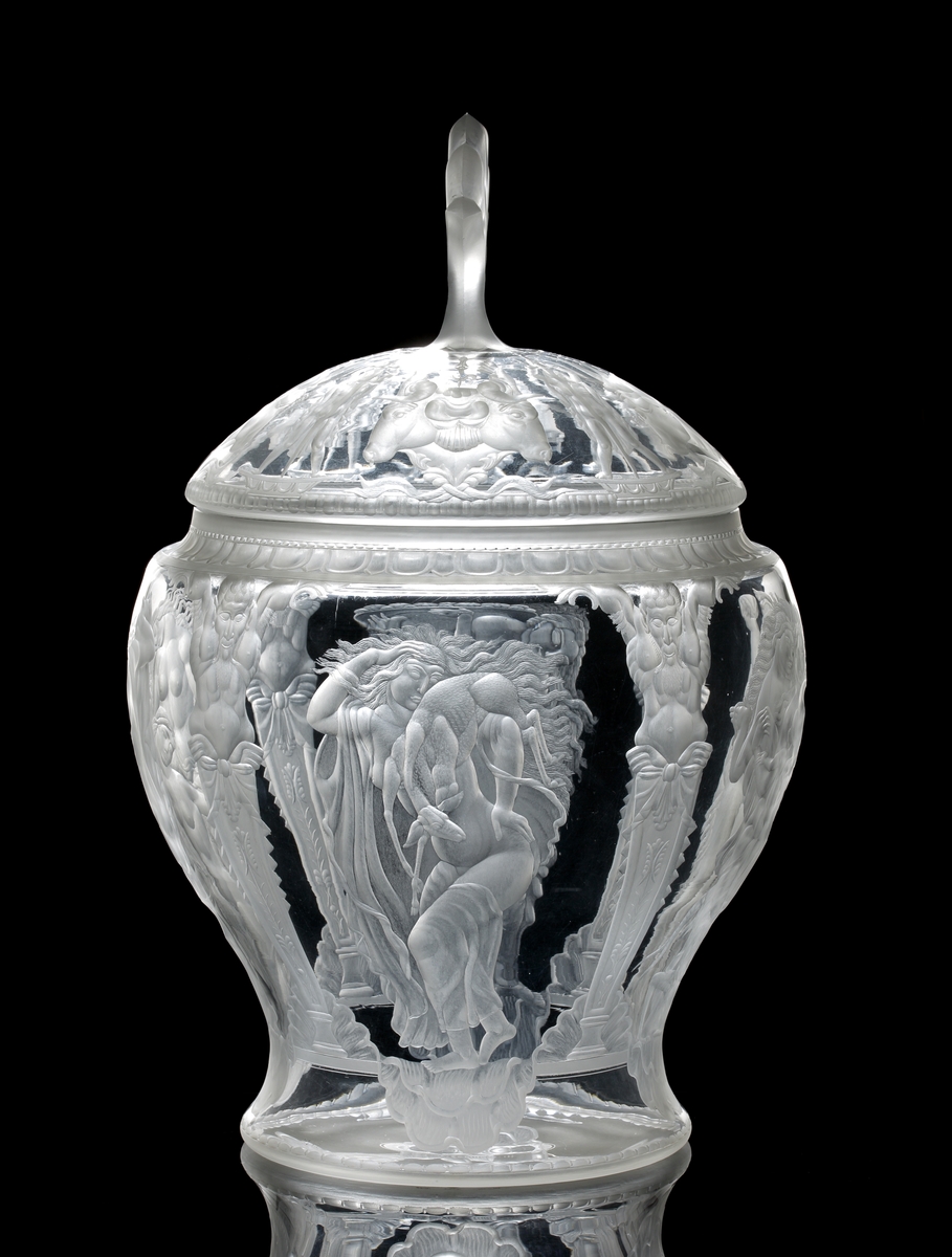 Formgiven av Simon Gate, gravyrarbete utfört av Gustav Abels. "Oxhuvudena", stor urna (eller pokal) med lock. Gravyr med motiv består av fyra scener, samtliga innehållande kvinnor i olika scener, och i en scen finns även ett barn. Dessa motiv ramas in av fyra graverade pelare, vilka uppåt avslutas med en mytologisk gestalt. Locket graverat motiv bestående av tjurhuvuden i fyra grupper om två eller tre stycken huvuden. Mellan dessa människogestalter med svärd som sticks ner i marken. Överst en knopp i form av en plym.