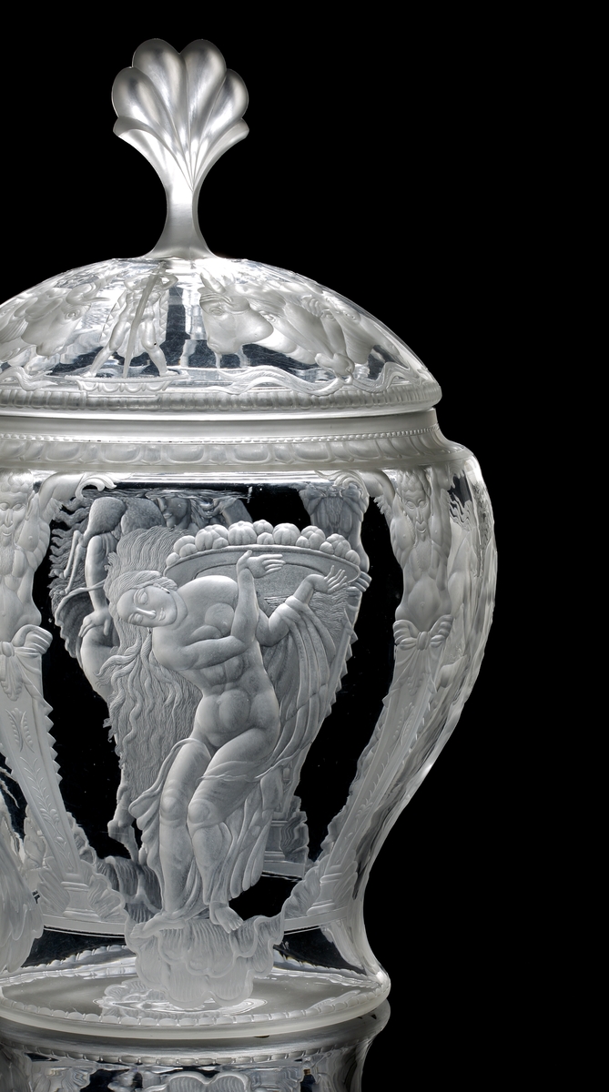 Formgiven av Simon Gate, gravyrarbete utfört av Gustav Abels. "Oxhuvudena", stor urna (eller pokal) med lock. Gravyr med motiv består av fyra scener, samtliga innehållande kvinnor i olika scener, och i en scen finns även ett barn. Dessa motiv ramas in av fyra graverade pelare, vilka uppåt avslutas med en mytologisk gestalt. Locket graverat motiv bestående av tjurhuvuden i fyra grupper om två eller tre stycken huvuden. Mellan dessa människogestalter med svärd som sticks ner i marken. Överst en knopp i form av en plym.