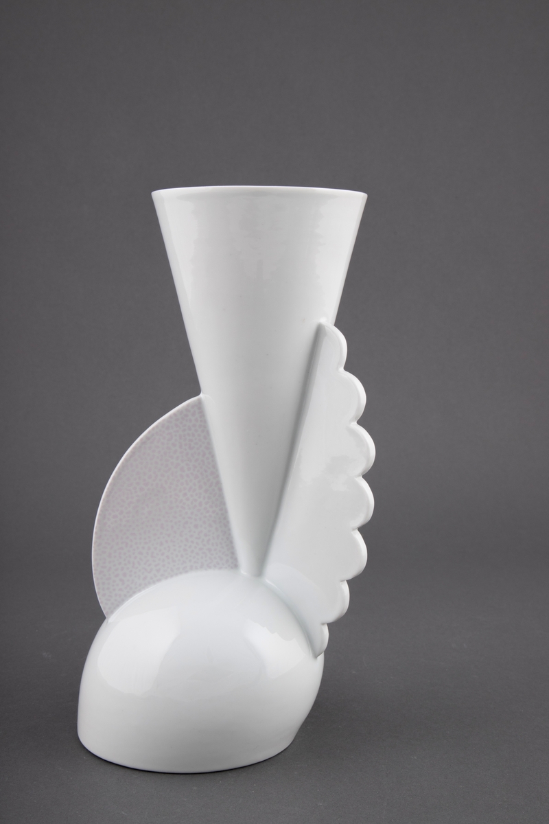 Vase i håndreid porselen med dekaler. Konisk korpus festet på en stor rund base. Vasen har to vinger på baksiden og en avrundet skive med rosa prikkemønster i fronten.