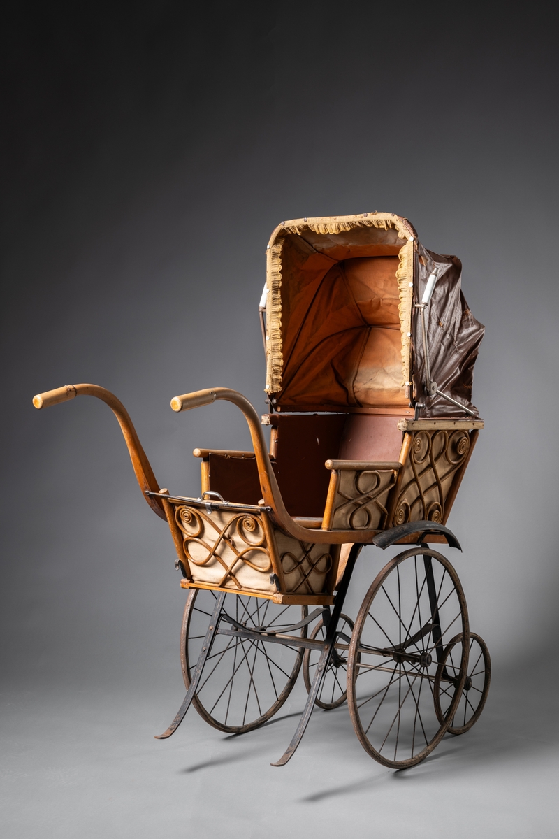 Barnvagn, kombinerad ligg- och sittvagn. Fotlådan går att fälla upp/ner till liggande respektive sittande läge. Stomme av järn bestående av underrede med två stora framhjul och två små bakhjul, samt två stödben (så att vagnen inte tippar fram). Hjulen är av trä med plåtskoning och ekrar av järn. Korg av trä, betsat, dekorerad utvändigt med böjd rotting. Invändigt fodrad med brunt konstläder. Stoppad sits. Två höga, böjda trähandtag. Sufflett av brunt konstläder på metallställning. Suffletten går att fälla upp och ner samt går att ta av. Handtag av vitt porslin. Runt sufflettens ytterkant är ett textilt band med udd fäst. Bandet har ursprungligen varit fäst med nubb, senare fäst med häftstift (de två översta på höger sida i samband med registreringen). Band av textil runt kanten under suffletten.  Sits och fotlådan nötta, skador på suffletten.