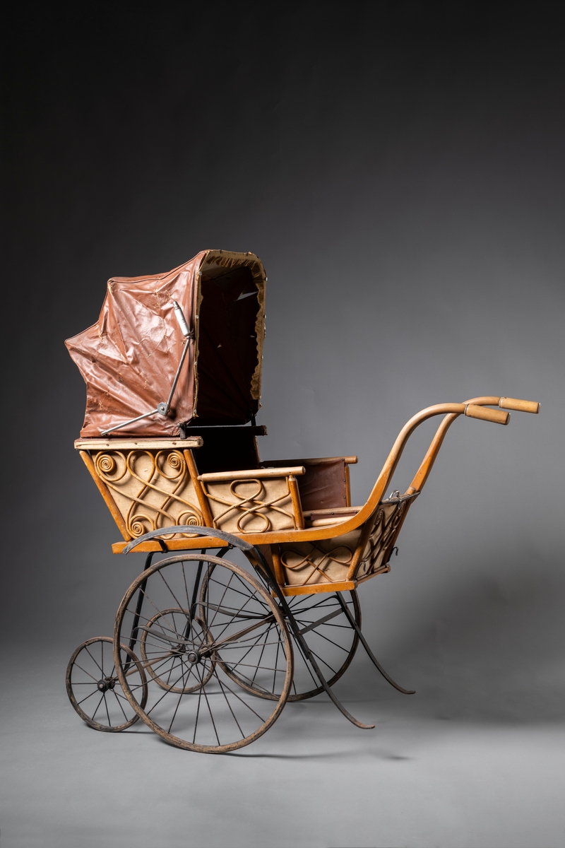 Barnvagn, kombinerad ligg- och sittvagn. Fotlådan går att fälla upp/ner till liggande respektive sittande läge. Stomme av järn bestående av underrede med två stora framhjul och två små bakhjul, samt två stödben (så att vagnen inte tippar fram). Hjulen är av trä med plåtskoning och ekrar av järn. Korg av trä, betsat, dekorerad utvändigt med böjd rotting. Invändigt fodrad med brunt konstläder. Stoppad sits. Två höga, böjda trähandtag. Sufflett av brunt konstläder på metallställning. Suffletten går att fälla upp och ner samt går att ta av. Handtag av vitt porslin. Runt sufflettens ytterkant är ett textilt band med udd fäst. Bandet har ursprungligen varit fäst med nubb, senare fäst med häftstift (de två översta på höger sida i samband med registreringen). Band av textil runt kanten under suffletten.  Sits och fotlådan nötta, skador på suffletten.