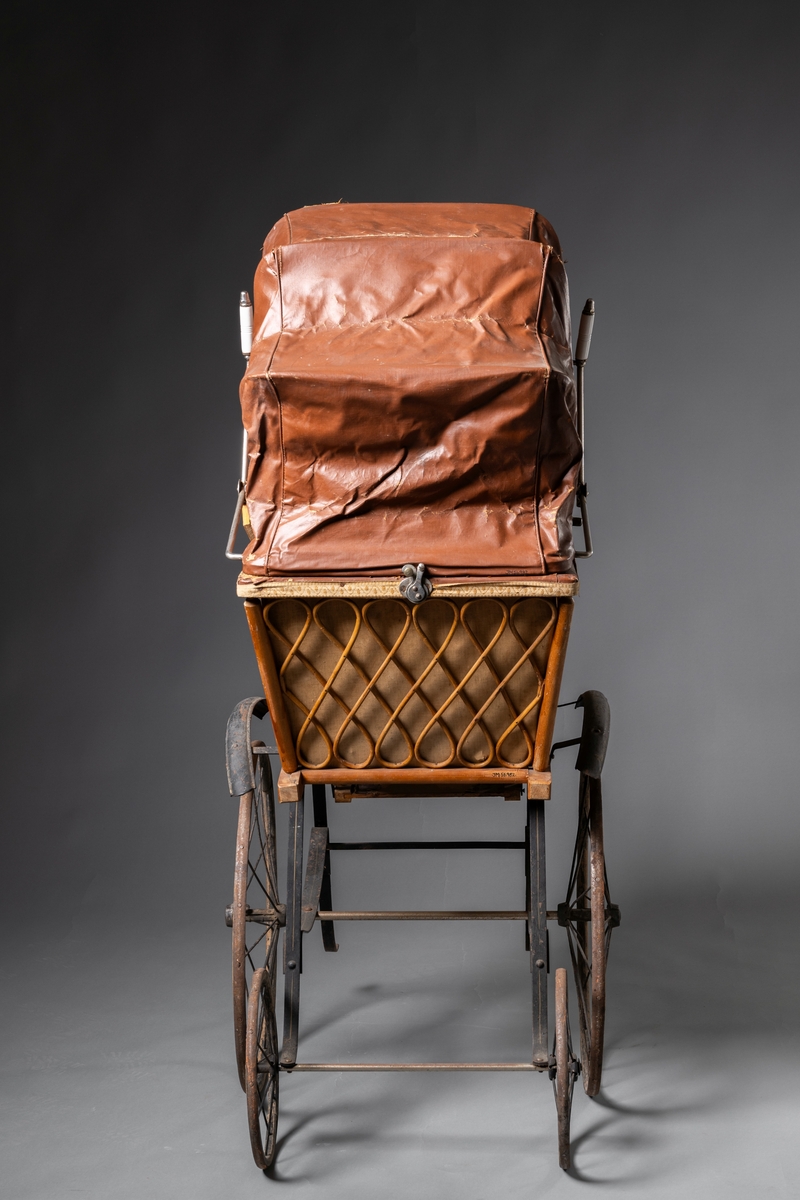 Barnvagn, kombinerad ligg- och sittvagn. Fotlådan går att fälla upp/ner till liggande respektive sittande läge. Stomme av järn bestående av underrede med två stora framhjul och två små bakhjul, samt två stödben (så att vagnen inte tippar fram). Hjulen är av trä med plåtskoning och ekrar av järn. Korg av trä, betsat, dekorerad utvändigt med böjd rotting. Invändigt fodrad med brunt konstläder. Stoppad sits. Två höga, böjda trähandtag. Sufflett av brunt konstläder på metallställning. Suffletten går att fälla upp och ner samt går att ta av. Handtag av vitt porslin. Runt sufflettens ytterkant är ett textilt band med udd fäst. Bandet har ursprungligen varit fäst med nubb, senare fäst med häftstift (de två översta på höger sida i samband med registreringen). Band av textil runt kanten under suffletten.  Sits och fotlådan nötta, skador på suffletten.