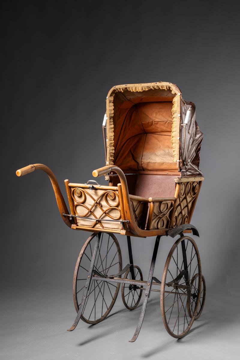 Barnvagn, kombinerad ligg- och sittvagn. Fotlådan går att fälla upp/ner till liggande respektive sittande läge. Stomme av järn bestående av underrede med två stora framhjul och två små bakhjul, samt två stödben (så att vagnen inte tippar fram). Hjulen är av trä med plåtskoning och ekrar av järn. Korg av trä, betsat, dekorerad utvändigt med böjd rotting. Invändigt fodrad med brunt konstläder. Stoppad sits. Två höga, böjda trähandtag. Sufflett av brunt konstläder på metallställning. Suffletten går att fälla upp och ner samt går att ta av. Handtag av vitt porslin. Runt sufflettens ytterkant är ett textilt band med udd fäst. Bandet har ursprungligen varit fäst med nubb, senare fäst med häftstift (de två översta på höger sida i samband med registreringen). Band av textil runt kanten under suffletten.  Sits och fotlådan nötta, skador på suffletten.