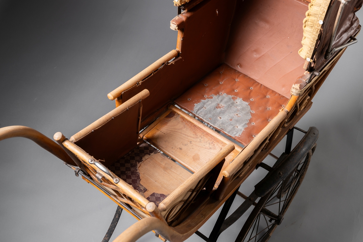 Barnvagn, kombinerad ligg- och sittvagn. Fotlådan går att fälla upp/ner till liggande respektive sittande läge. Stomme av järn bestående av underrede med två stora framhjul och två små bakhjul, samt två stödben (så att vagnen inte tippar fram). Hjulen är av trä med plåtskoning och ekrar av järn. Korg av trä, betsat, dekorerad utvändigt med böjd rotting. Invändigt fodrad med brunt konstläder. Stoppad sits. Två höga, böjda trähandtag. Sufflett av brunt konstläder på metallställning. Suffletten går att fälla upp och ner samt går att ta av. Handtag av vitt porslin. Runt sufflettens ytterkant är ett textilt band med udd fäst. Bandet har ursprungligen varit fäst med nubb, senare fäst med häftstift (de två översta på höger sida i samband med registreringen). Band av textil runt kanten under suffletten.  Sits och fotlådan nötta, skador på suffletten.