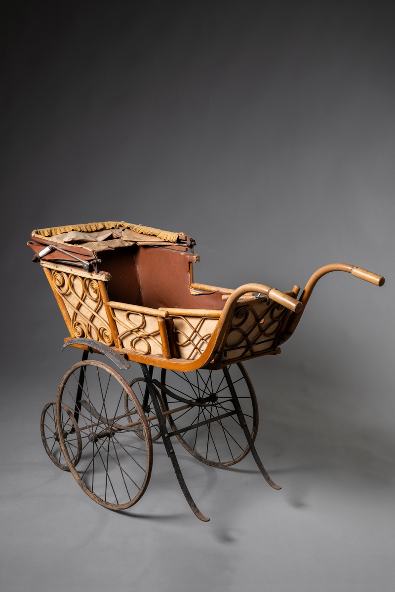 Barnvagn, kombinerad ligg- och sittvagn. Fotlådan går att fälla upp/ner till liggande respektive sittande läge. Stomme av järn bestående av underrede med två stora framhjul och två små bakhjul, samt två stödben (så att vagnen inte tippar fram). Hjulen är av trä med plåtskoning och ekrar av järn. Korg av trä, betsat, dekorerad utvändigt med böjd rotting. Invändigt fodrad med brunt konstläder. Stoppad sits. Två höga, böjda trähandtag. Sufflett av brunt konstläder på metallställning. Suffletten går att fälla upp och ner samt går att ta av. Handtag av vitt porslin. Runt sufflettens ytterkant är ett textilt band med udd fäst. Bandet har ursprungligen varit fäst med nubb, senare fäst med häftstift (de två översta på höger sida i samband med registreringen). Band av textil runt kanten under suffletten.  Sits och fotlådan nötta, skador på suffletten.