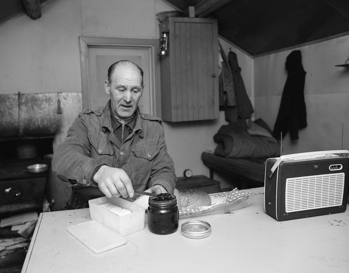 Skogsarbeider Johan Rasch spiser frokost i Smaltjernkoia i Svartholtet, Elverum, Hedmark i januar 1975.