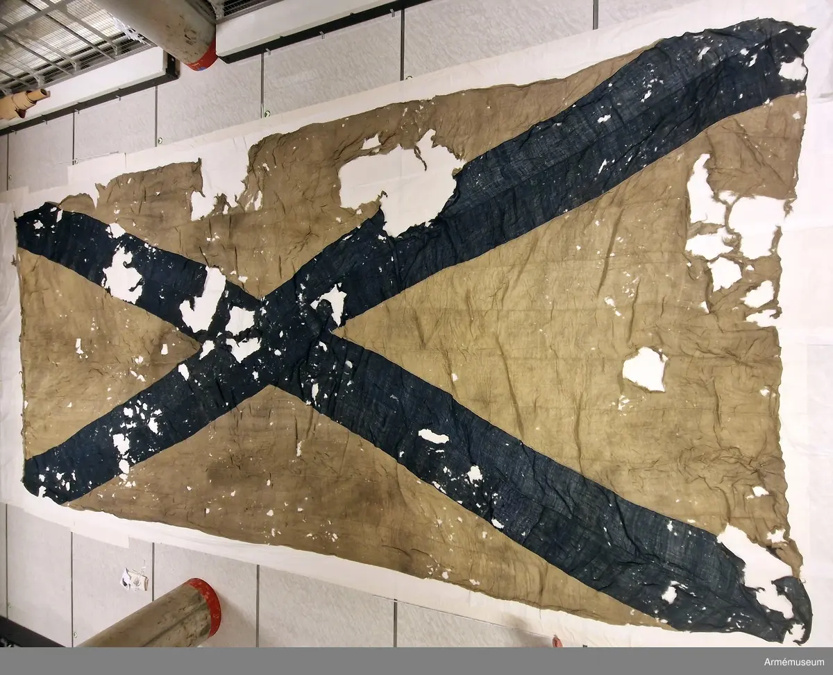 Flagga av flaggduk, sydd av 11 våder vitt tyg samt två våder blått i ett S:t Andreaskors. Vid stångsidan en förstärkning med snören som ska fästa flaggan i riggen. Även själva flaggan är förstärkt med extra lager blått tyg närmast stångsidan. En liten symbol broderad i vitt på det blå fältet.
Etikett av pergament med text: "No 19, Denna Ryska Flagga 11 Duk, är tagen uti Bataillen vid Svensksund under Hans Kungl. Maj:ts Egit Höga Befäl och Anförande 9. Juli 1790".