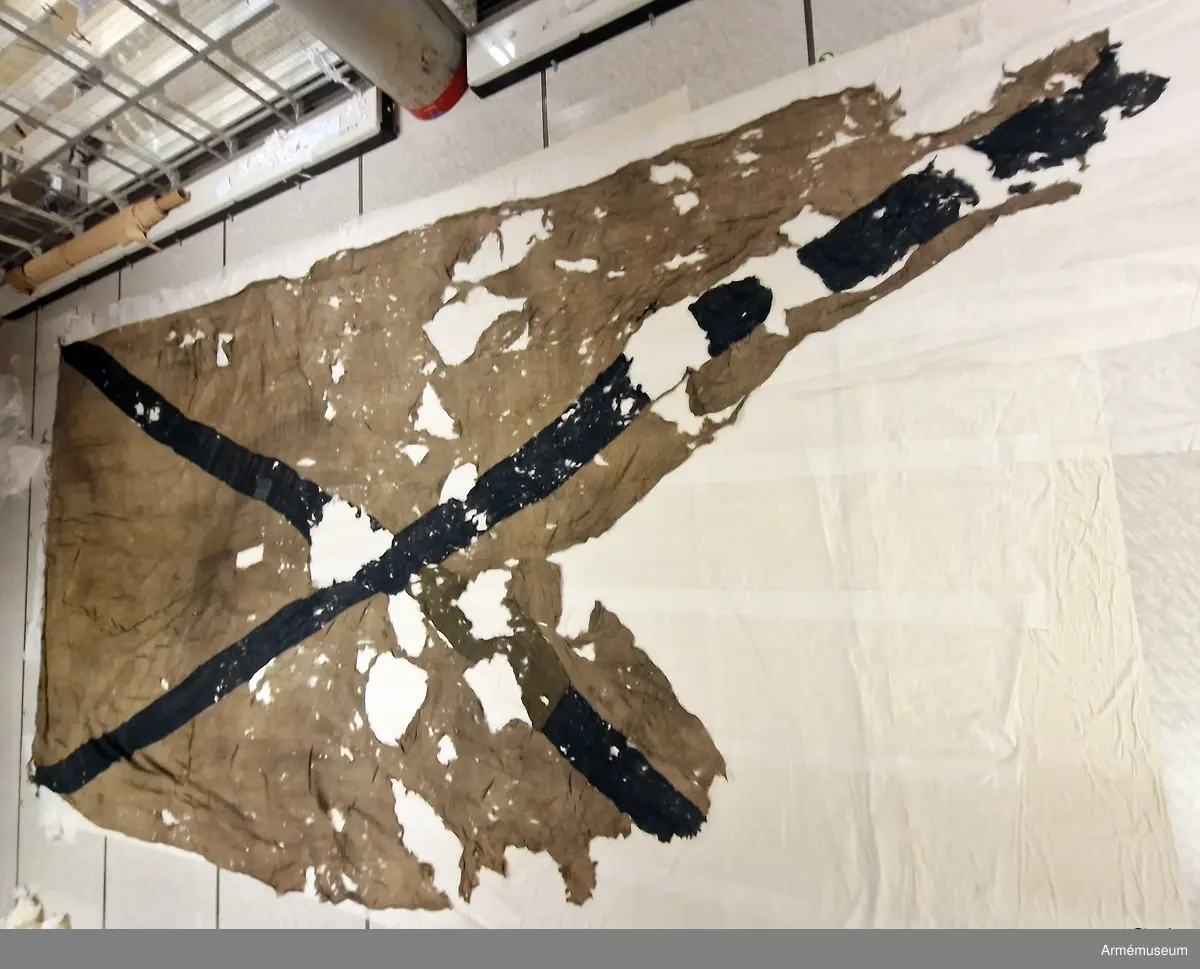 Flagga av flaggduk, vit med blått S:t Andreaskors. Vid stångsidan en förstärkning med snören som ska fästa flaggan i riggen. Även själva standerten är förstärkt med extra lager blått tyg närmast stångsidan.
Etikett av pergament med text: "Denna Ryska Flagg. 13 duk, är tagen uti Bataillen vid Svensksund under Hans Kungl. Maj:ts Egit Höga Befäl och Anförande. den 9. Juli 1790. No 27".