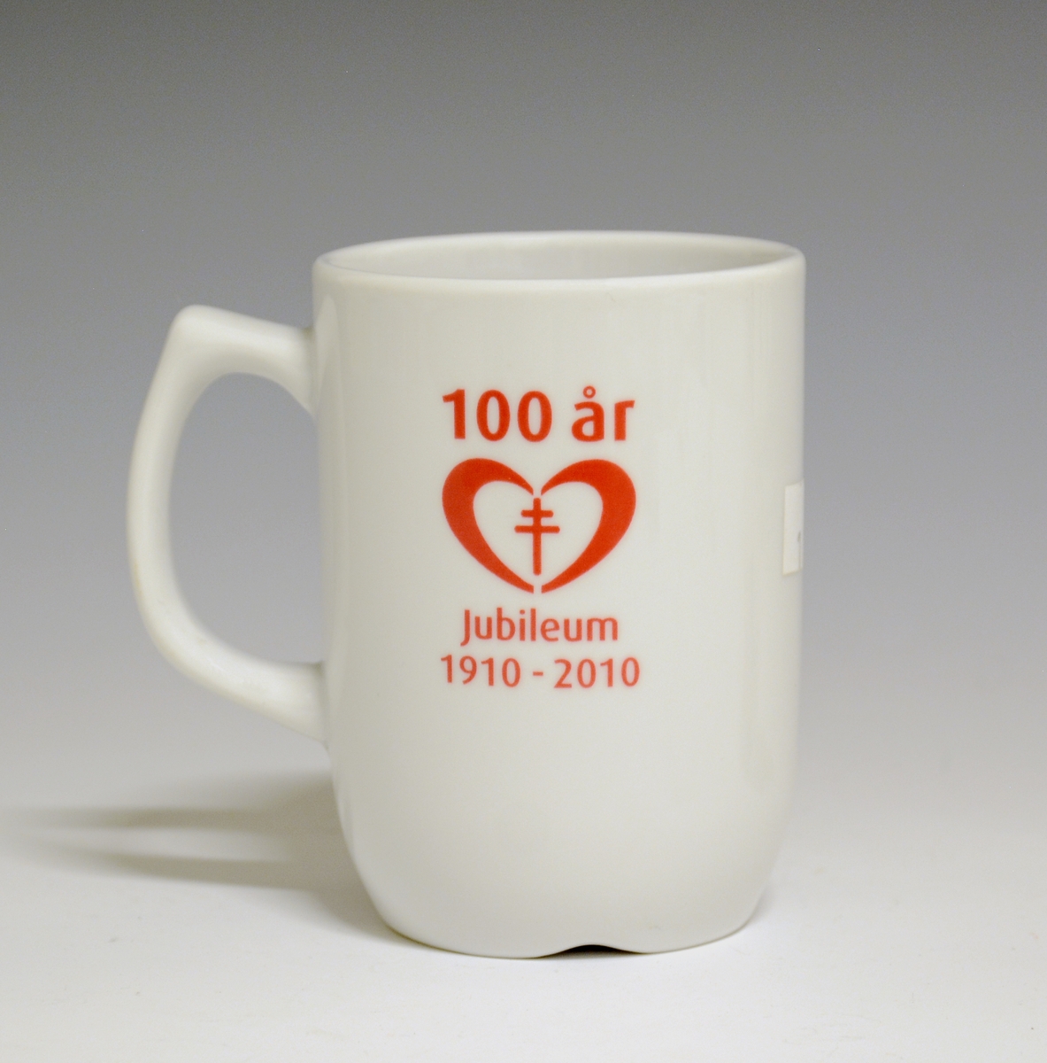 Krus av porselen med  hvit glasur. Påskriften "Nasjonalforeningen for folkehelsen 100 år 1910-2010" i rødt på begge sider av kruset.
Modell: Form av Tias Eckhoff
