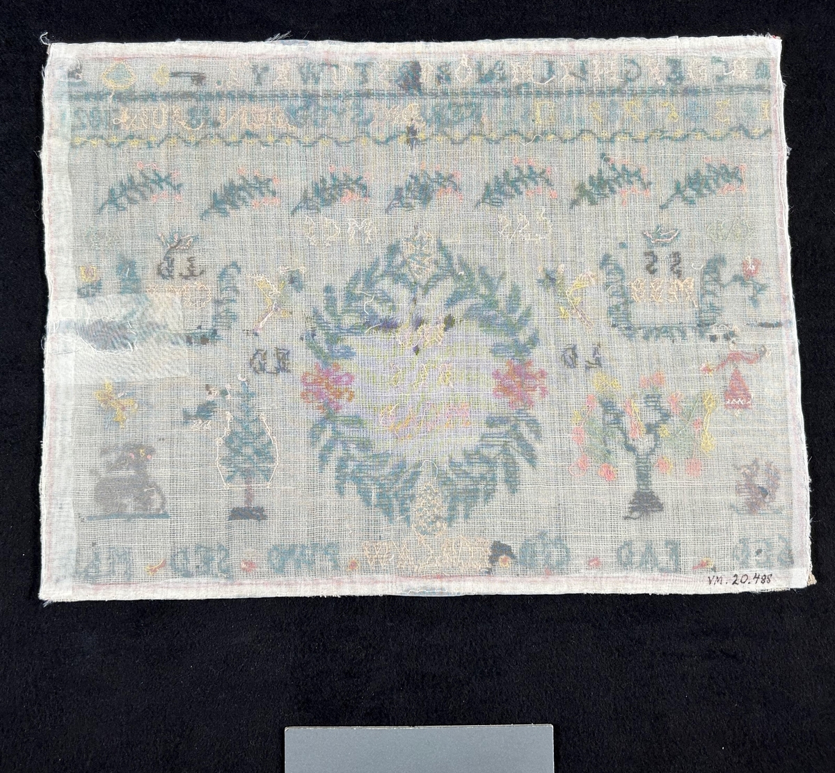 Märkduk i symmetrisk komposition. Överst två rader med alfabetet och siffror. På den undre raden står "Ferdigsydd den 18 juli 1821." I mitten en oval krans med monogram; JPD, BLLS, MCAD, på båda sior två par krönta monogram SS, MBB LD, CMB. Längst ned en rad med olika monogram; SLD, FAD, CJD, ECB, CAW, PWD, SED, MLD. För övrigt växt- och djurmotiv. Monterad på papper.
