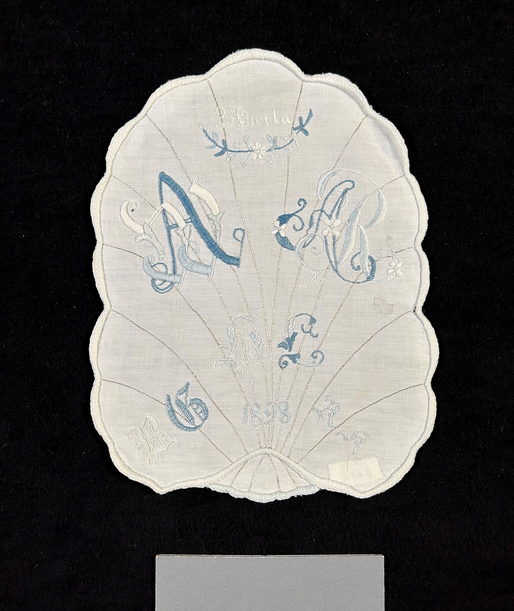 Märkduk av vitt linne med formen av ett blad med nerver av beige silke i stjälksöm. Allt märkt i blått och vitt märkgarn. Vit langett runt om.