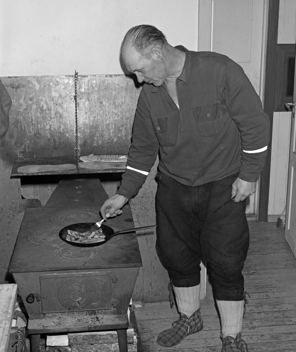 Skogsarbeider lager middag i koia. Johan Rasch steker flesk og poteter i Smaltjernkoia i Svartholtet, Elverum, Hedmark i januar 1975.