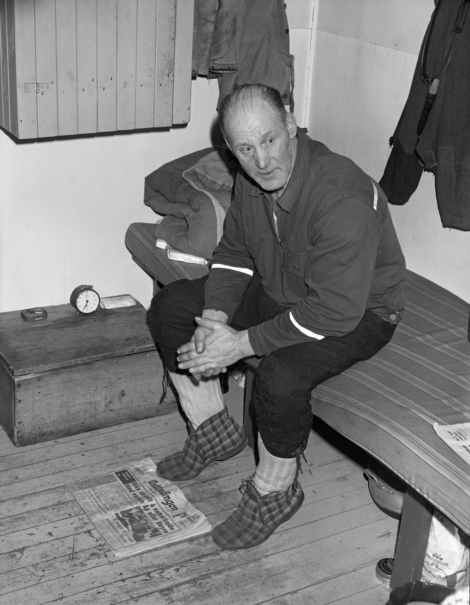 Skogsarbeider hviler i koia. Johan Rasch sitter i senga si i Smaltjernkoia i Svartholtet, Elverum, Hedmark i januar 1975.