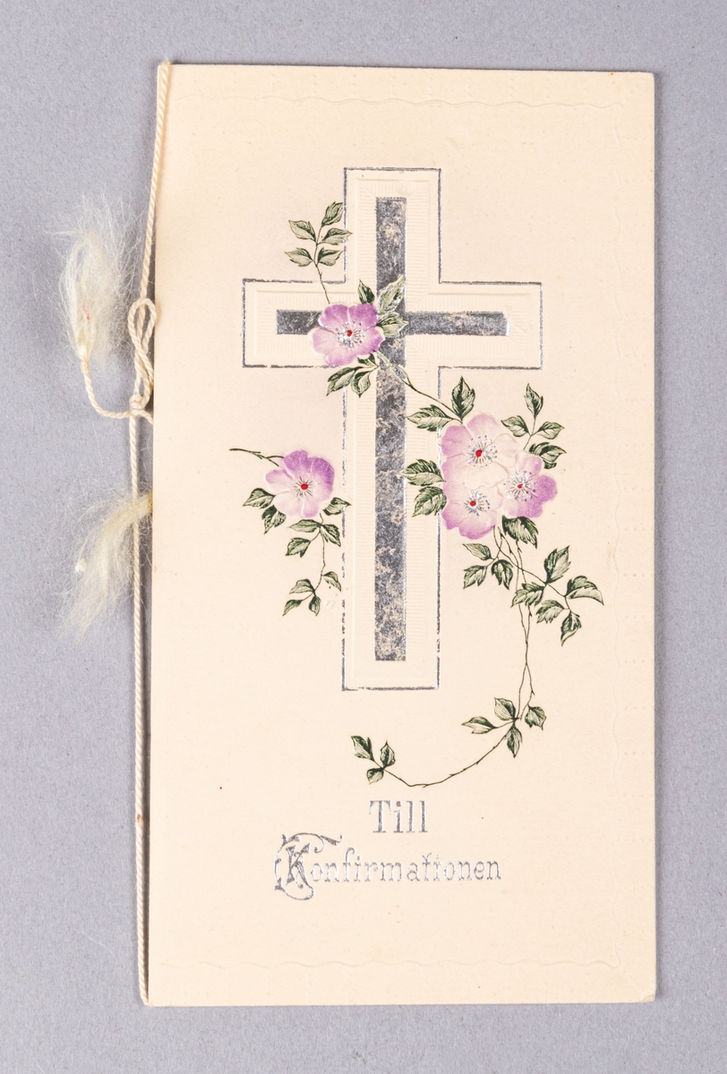 Konfirmationskort. På framsidan i relief, blommor i violett och grönt. Kors och text "Till konfirmationen" i silver. På insidan bild av Jesus. Tryckt text och skriven text. Vit snodd.