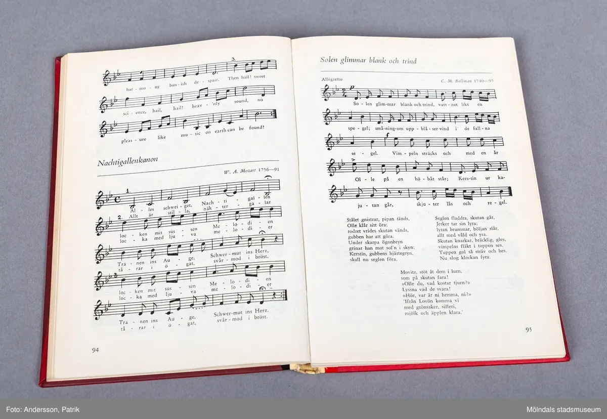 En inbunden sångbok, Framsidan är mörkröd och pryds av en stor not i en ljusare röd färg. 
Längst ned står det Musik med svarta bokstäver. Pärmens rygg är ljusare röd.