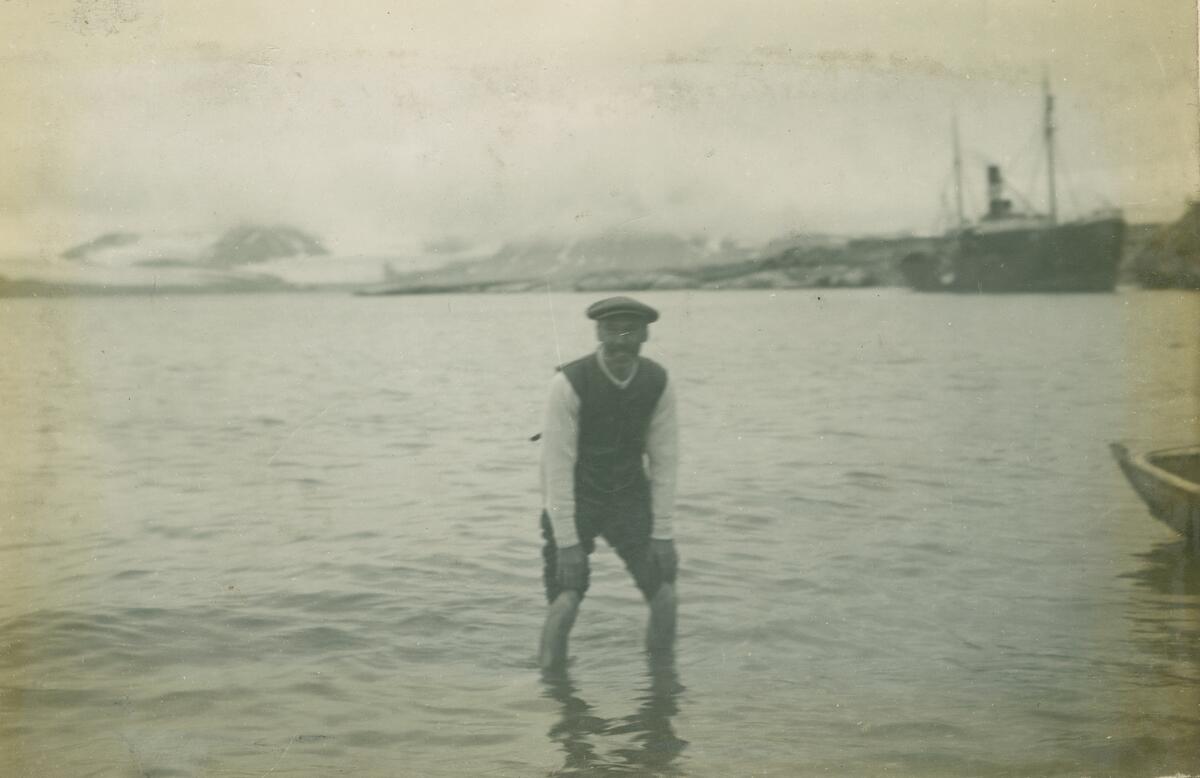 En mann står i sjøen i Ny-London på Blomstrandhalvøya. Fraktebåten Activ på kaia i bakgrunn. Gjenstandsnummer SVB 2101