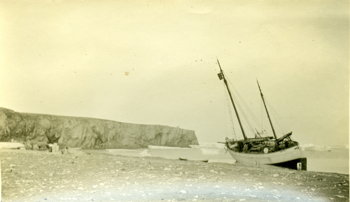 Seilskute på Svalbard 1914/15. Bilde fra Jens Kristoffer Bays bildesamling. Han var vinteren 1914/15 sjef for en overvintringsekspedisjon på Svalbard, og det er mulig at bildet er fra denne ekspedisjonen. Båten ligger i fjæra, det er kasser og utstyr på land.