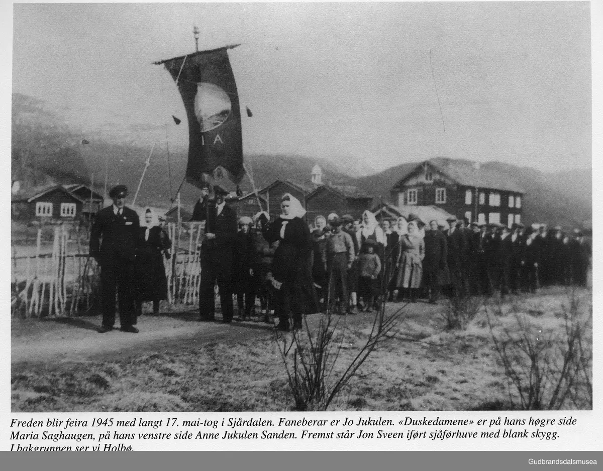 Freden blir feira 1945 med langt 17.mai-tog i Sjårdalen. Faneberar er Jo Jukulen. Duskedamene er på hans høgre side Maria Saghaugen, på hans venstre side Anne Jukulen Sanden. Fremst står Jon Sveen iført sjåførhuve med blank skygg. I bakgrunnen ser vi Holbø.
utlån: Magnar Bråten

Vågåkalenderen 1996, utgjevar: Vågå Kameraklubb