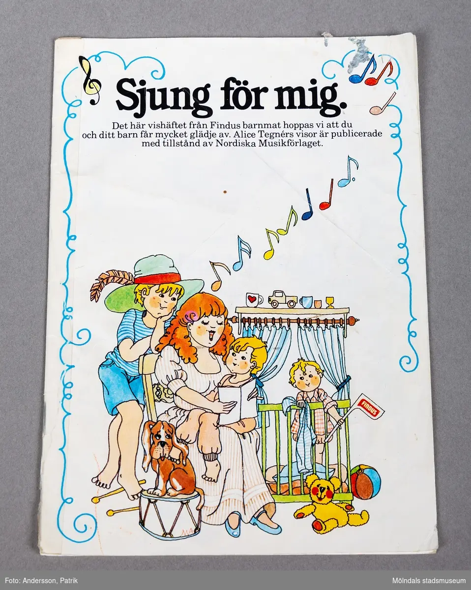 Ett tunnt häfte med barnsånger.
Framsidan är vit med svart huvudrubrik. Det finns en tecknad bild med en kvinna som sitter på en stol med ett barn i knäet. Hon håller i en bok och det kommer färglada tecknade toner från kvinnan. Bakom henne står ett större barn med en blå hatt med fjäder. I rummet finns också en hund på en trumma och ett barn i en hage. Det barnet håller i en flagga med texten Findus. En blå girlang omringar framsidan,
Inuti häftet finns färglagda teckningar och kända barnvisor av Alice Tegnér.